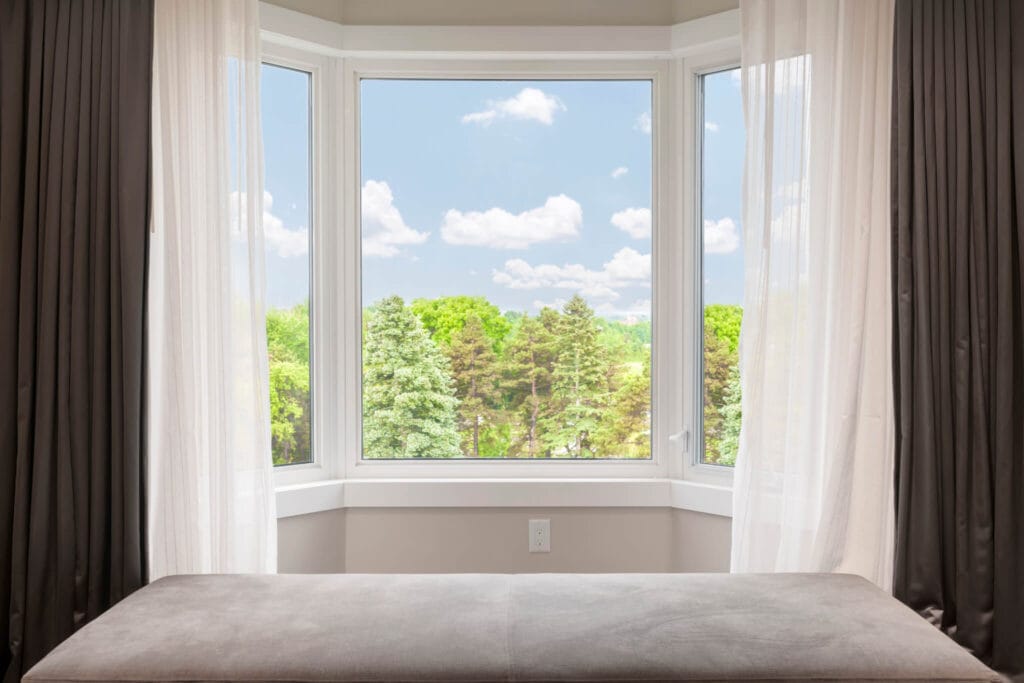 An interior shot of a bay window that has a view of beautiful trees and skyline.
