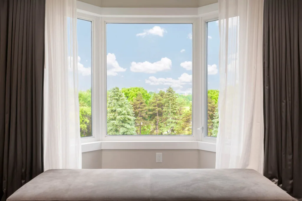 An interior shot of a bay window that has a view of beautiful trees and skyline.