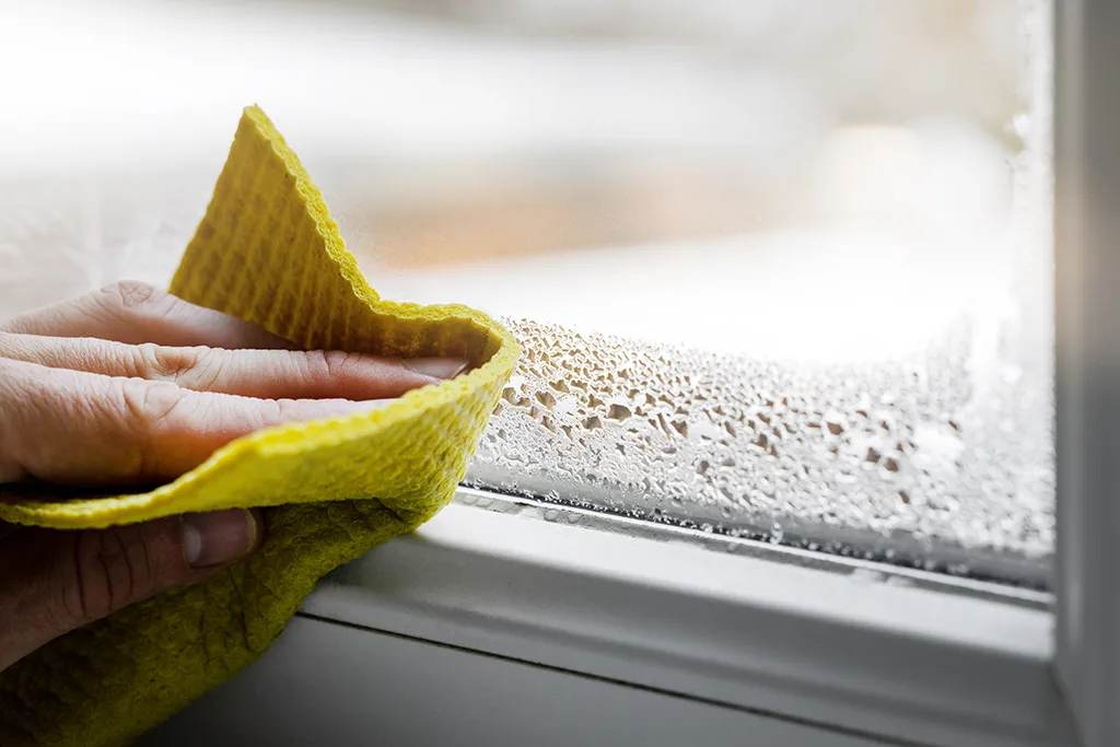 Cleaning window condensation with a yellow wash cloth.