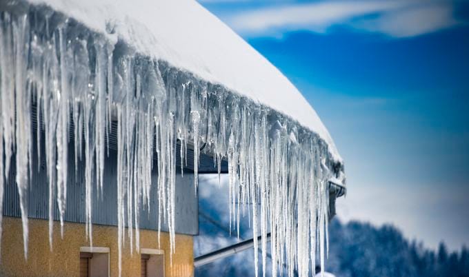 Roof with snow and icicles forming from an ice dam.